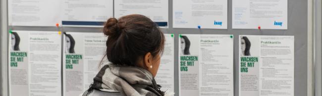 Eine Studentin steht vor einer Wand mit Stellenausschreibungen