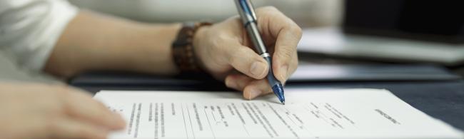 Die Hand eines Mannes, die einen Kuli hält und ein Formular auf einem Tisch ausfüllt